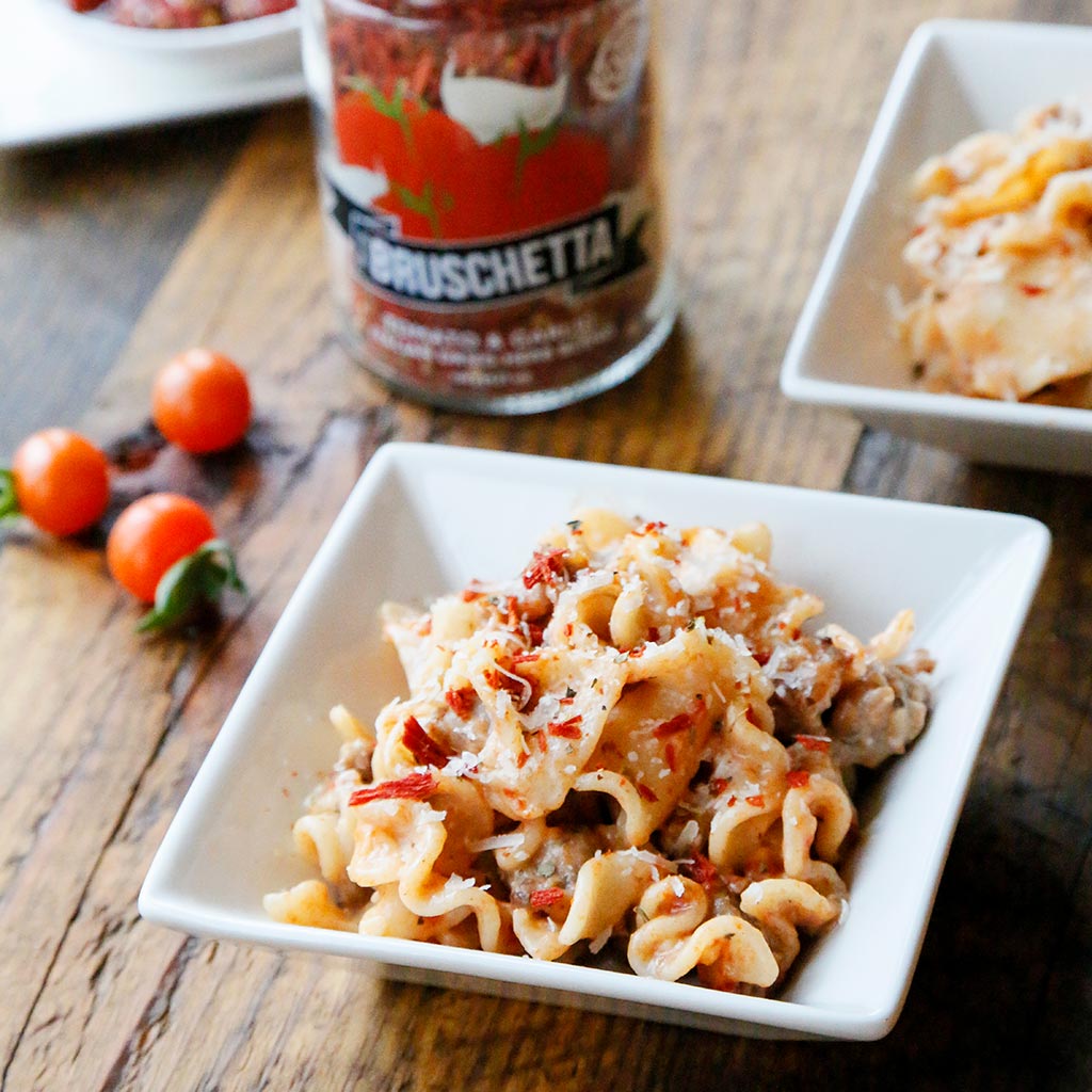 Drunken Bruschetta & Sausage Pasta made with Bruschetta Dried Herb Blend, Italian Extra Virgin Olive Oil and Italian Pasta served in a white bowl on a rustic wooden table.