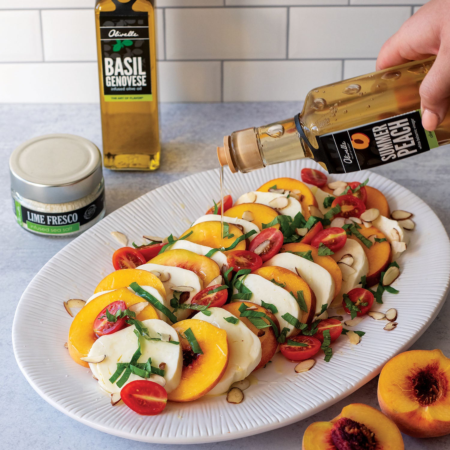 sliced peaches and mozzarella with basil, almonds, tomatoes, and peach balsamic vinegar served on a white platter next to peach vinegar and fresh, whole peaches