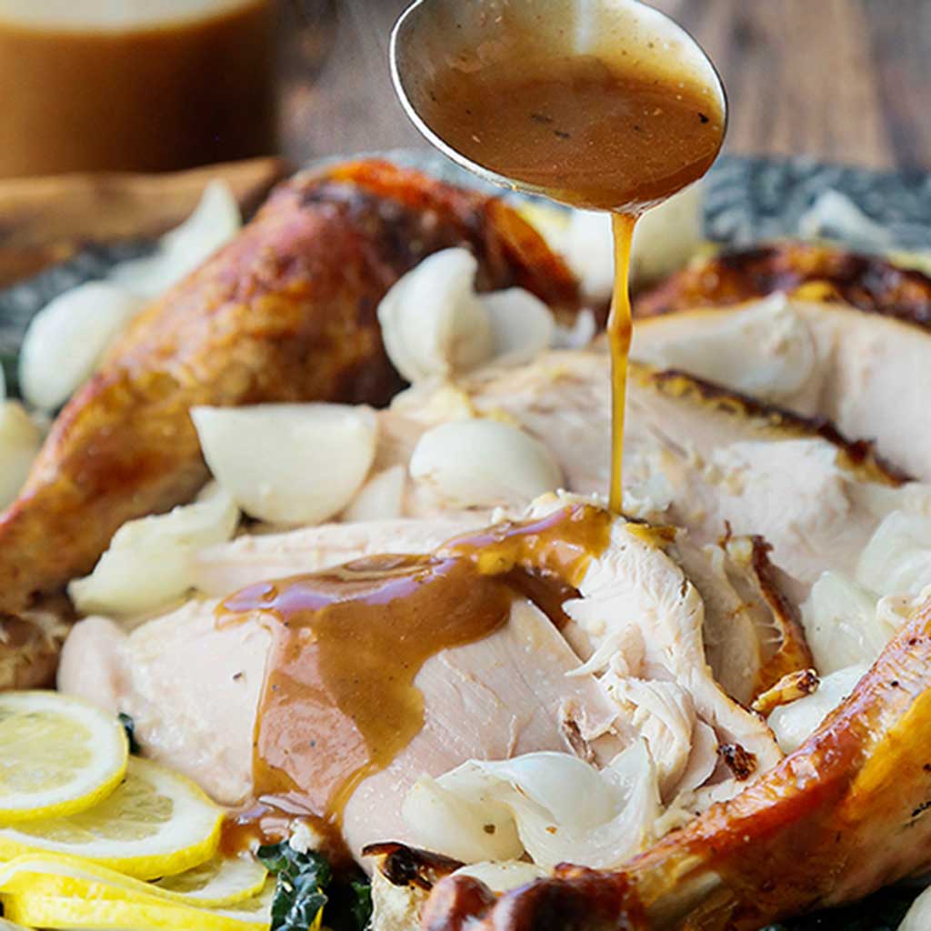 Balsamic Turkey Gravy drizzled over white turkey breast made with dark balsamic vinegar served next to lemon slices.