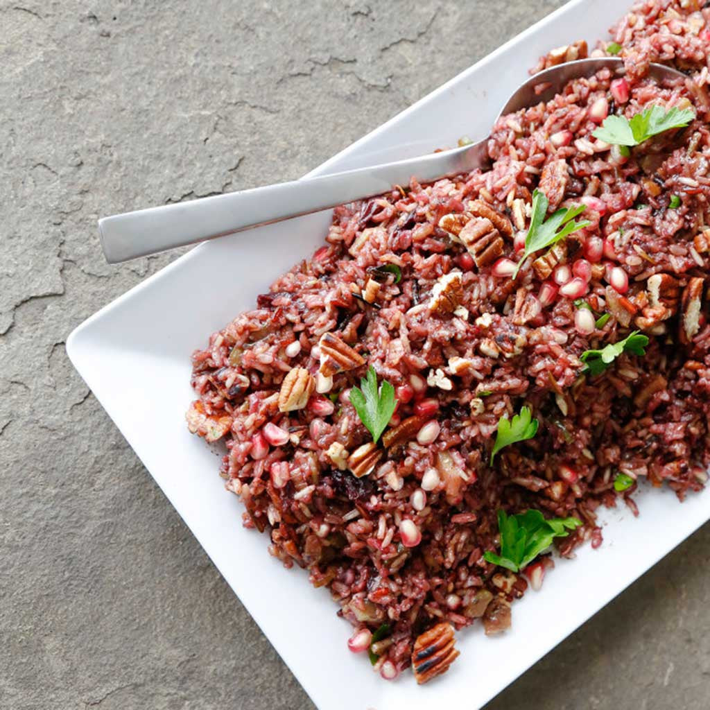 cherry and pomegranate wild rice salad served on a white serving platter with a spoon and garnished with parsley