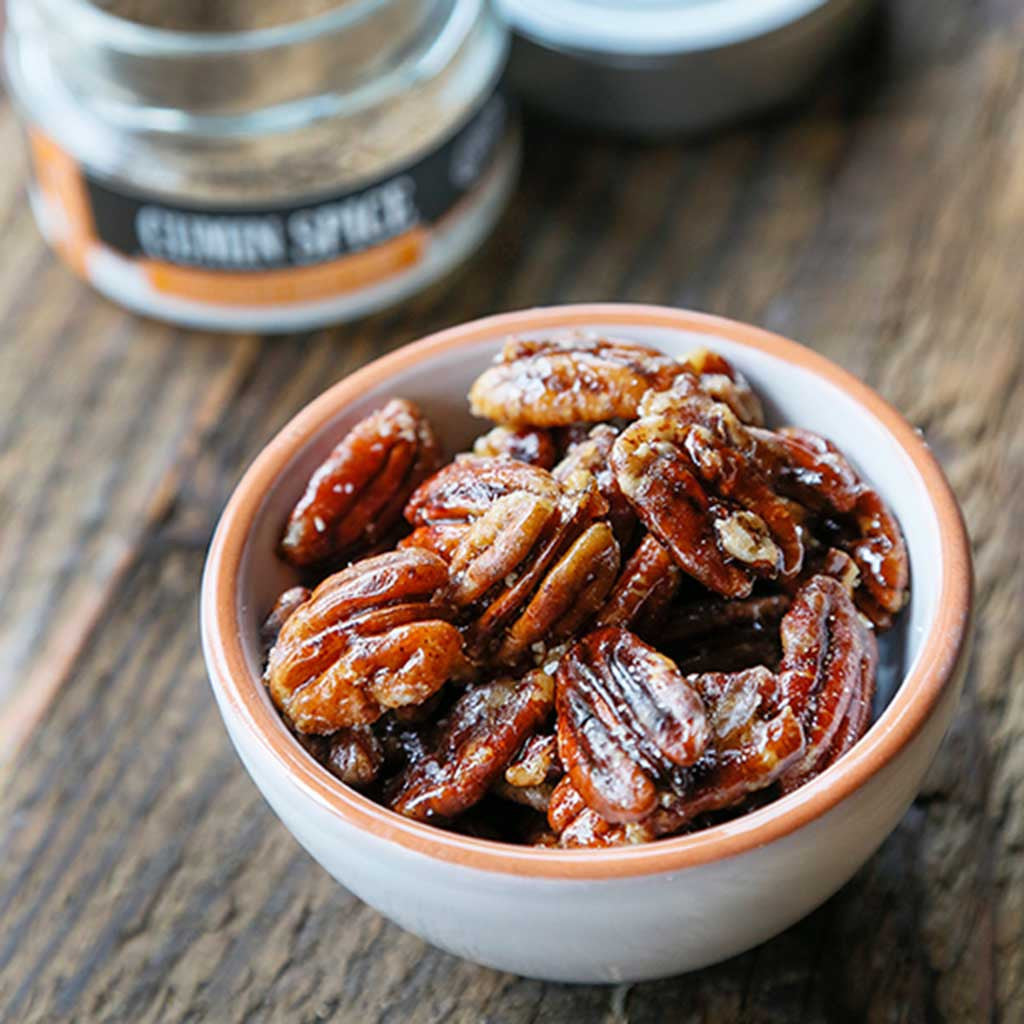 A cup of Cumin Maple Pecans topped with maple syrup and Cumin Spice Sea Salt served next to a jar of cumin spice infused sea salt 