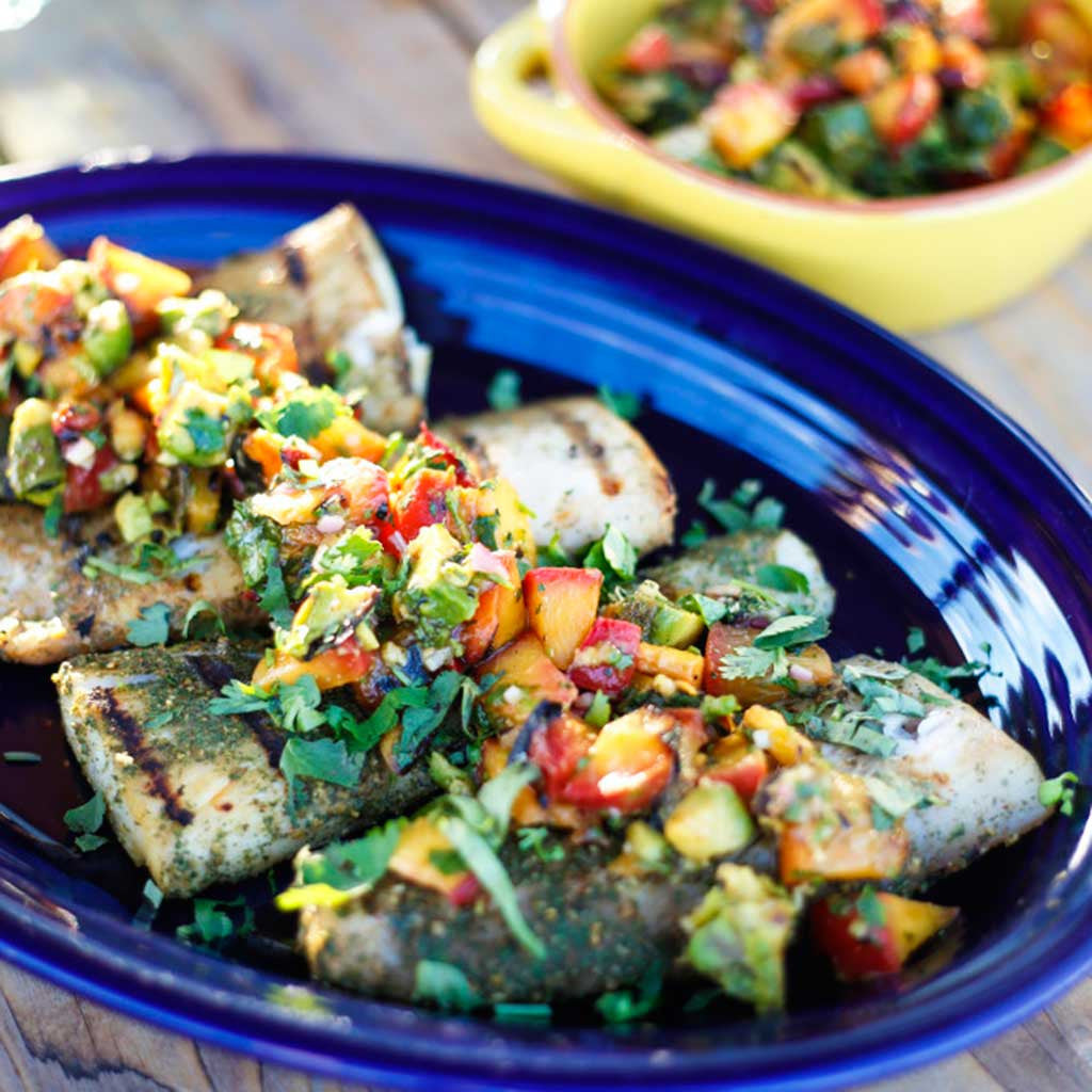 Fresh Mediterranean herb grilled fish with peach salsa served in a blue platter alongside a yellow bowl filled with peach salsa