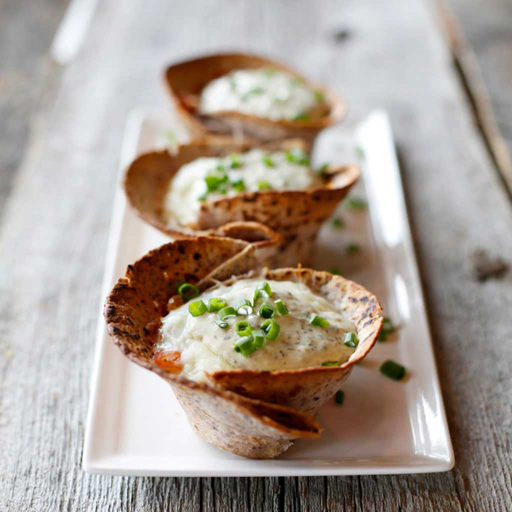 Delicious Mexican breakfast baskets topped with diced green chiles served on a white rectangular platter on a rustic board.