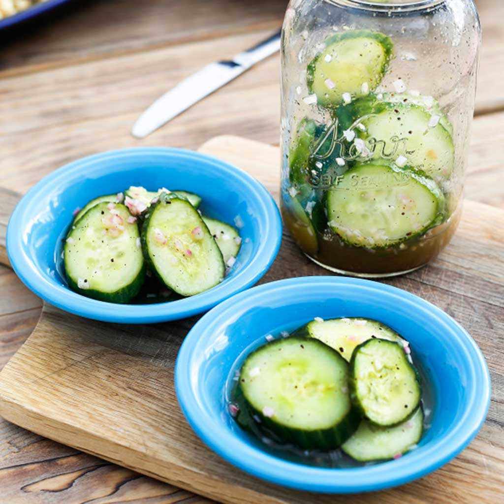 fresh citrus pickled cucumbers sliced in a blue bowl and in the jar served on a wooden platter