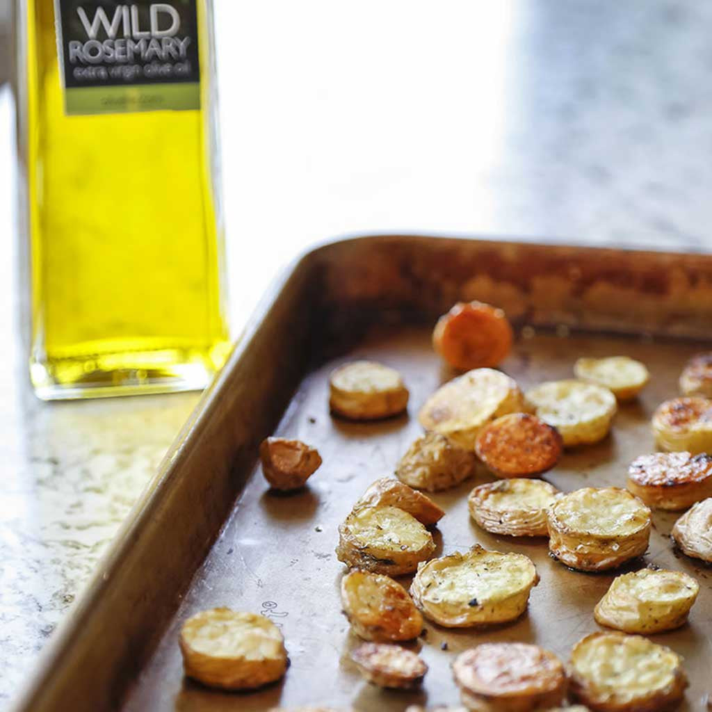 sliced roasted potatoes on baking sheet with wild rosemary olive oil served on a marble table top.