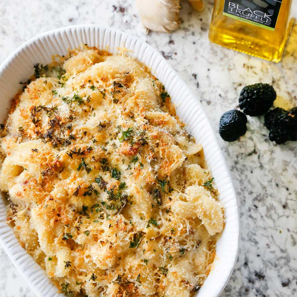 Truffled Mac and Cheese is the ultimate comfort food using avocado/black truffle olive oil, gruyere cheese and cheddar cheese to make it creamy and delicious. Served in a white platter on a granite table top next to black truffles.