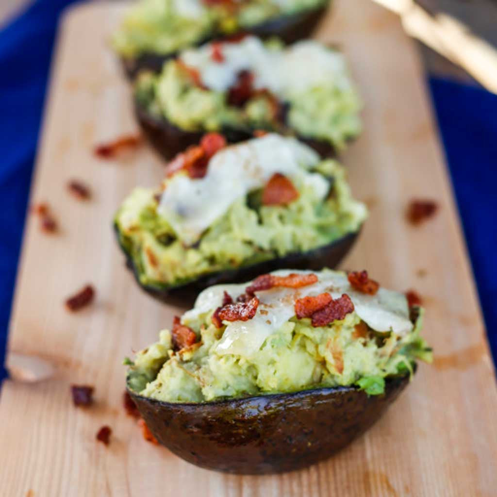 twice baked potatoes with avocado, bacon and manchego cheese garnished and served on a rustic wooden platter