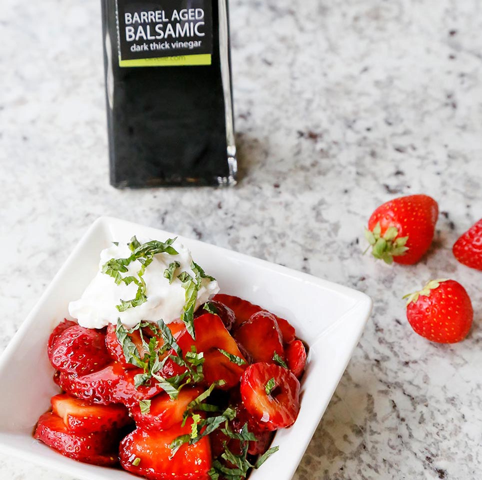 Barrel Aged Balsamic Strawberries made using our Barrel Aged Dark Balsamic Vinegar and sprinkled with Vanilla Bean Sea salt served in a white bowl on a marble counter top.