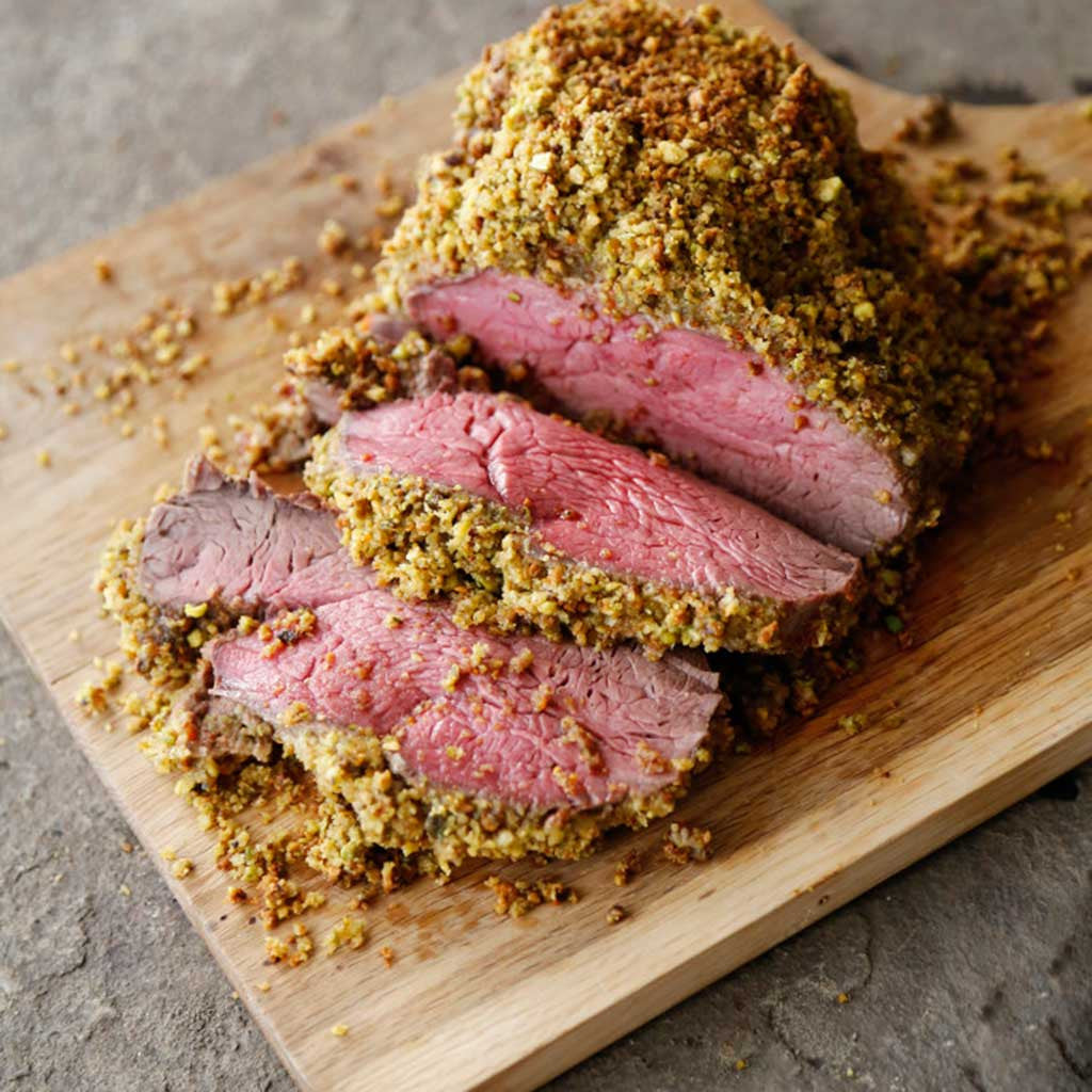 pistachio and Parmesan crusted beef tenderloin cooked perfectly to rare on a wooden cutting board