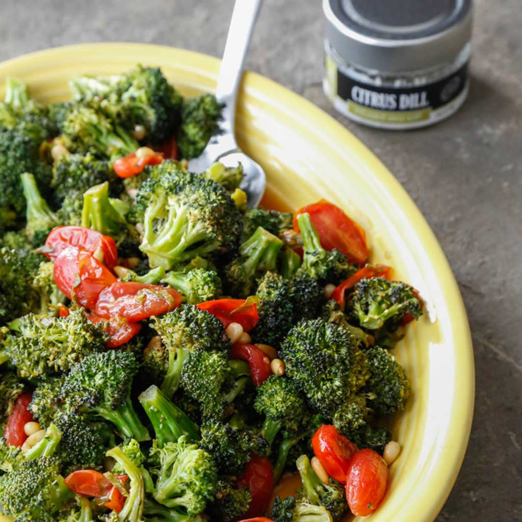 roasted broccoli with a warm tomato herb vinaigrette served on a yellow plate next to a jar of citrus dill sea salt 