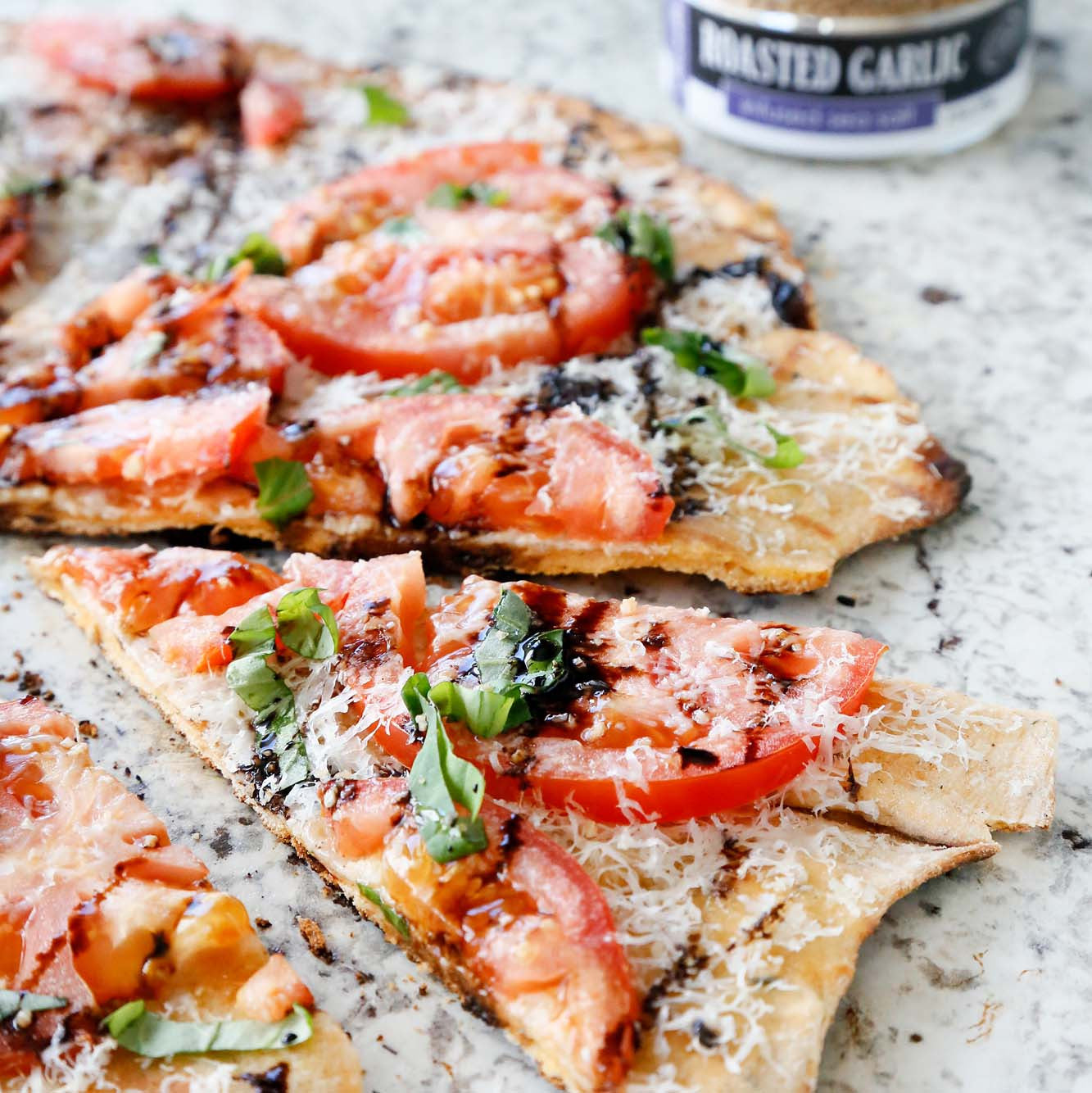Roasted Garlic Tomato Basil Pizza made with Wild Garlic Pizza Dough, Basil Olive Oil, pecorino cheese, tomatoes, basil and Roasted Garlic Sea Sea Salt served on a marble platter.