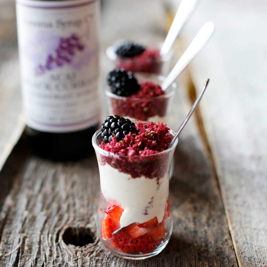 Spiced Italian Custard Parfaits with a Super-Food Crunch made from heavy cream, egg yolks and berries served three in a row on a wooden table top.