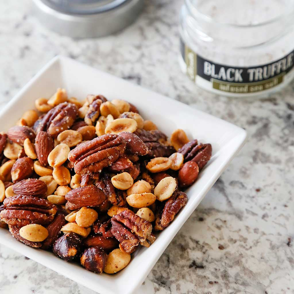 Truffle rosemary mixed nuts alongside black truffle sea salt plated on a marble counter top