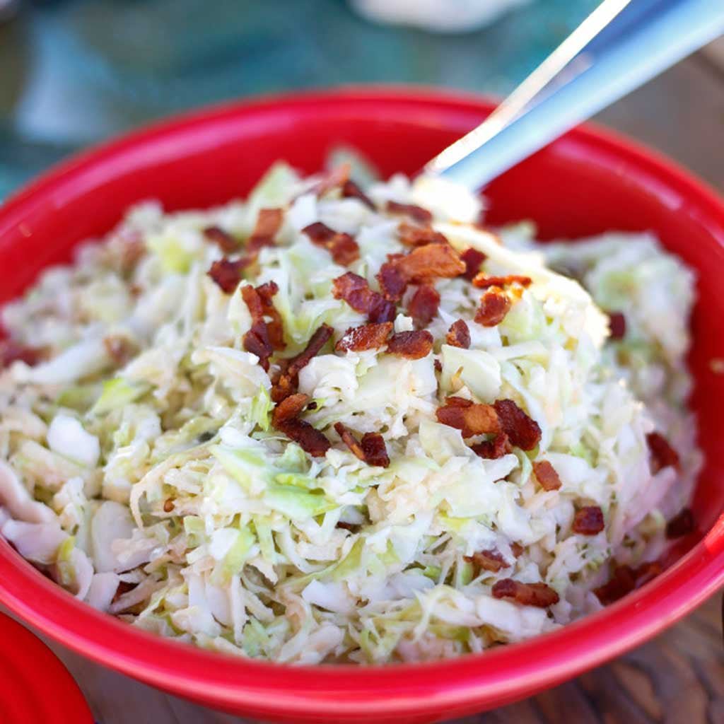 apple and cabbage coleslaw with greek yogurt citrus dressing in a red bowl and topped with bacon