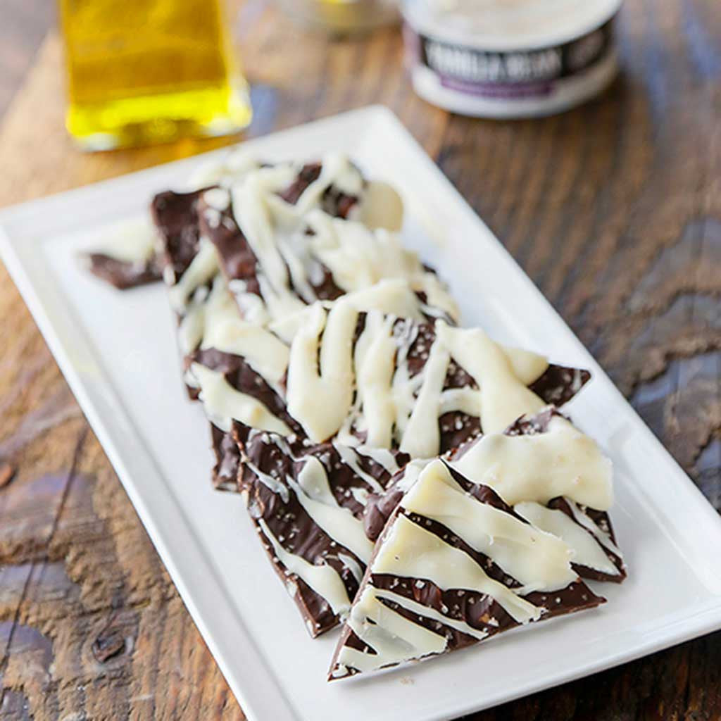 Blood Orange Chocolate Bark with White Chocolate drizzled on top served on a white, rectangular platter. Made with Blood Orange Infused Olive Oil and Vanilla Bean Sea Salt.
