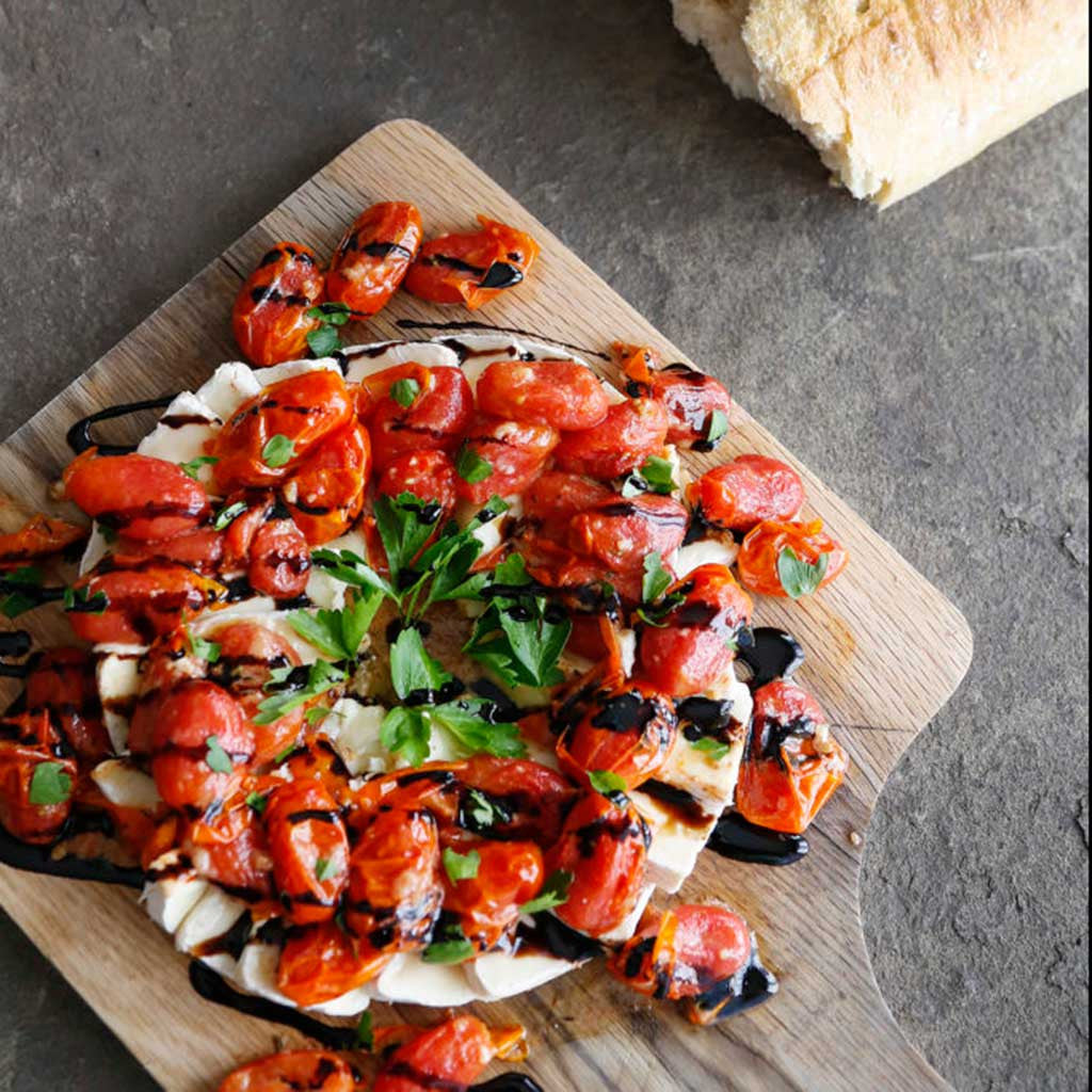 Warm brie topped with slow roasted tomatoes, a drizzle of dark barrel aged balsamic vinegar garnished with basil and served on a rustic wood platter