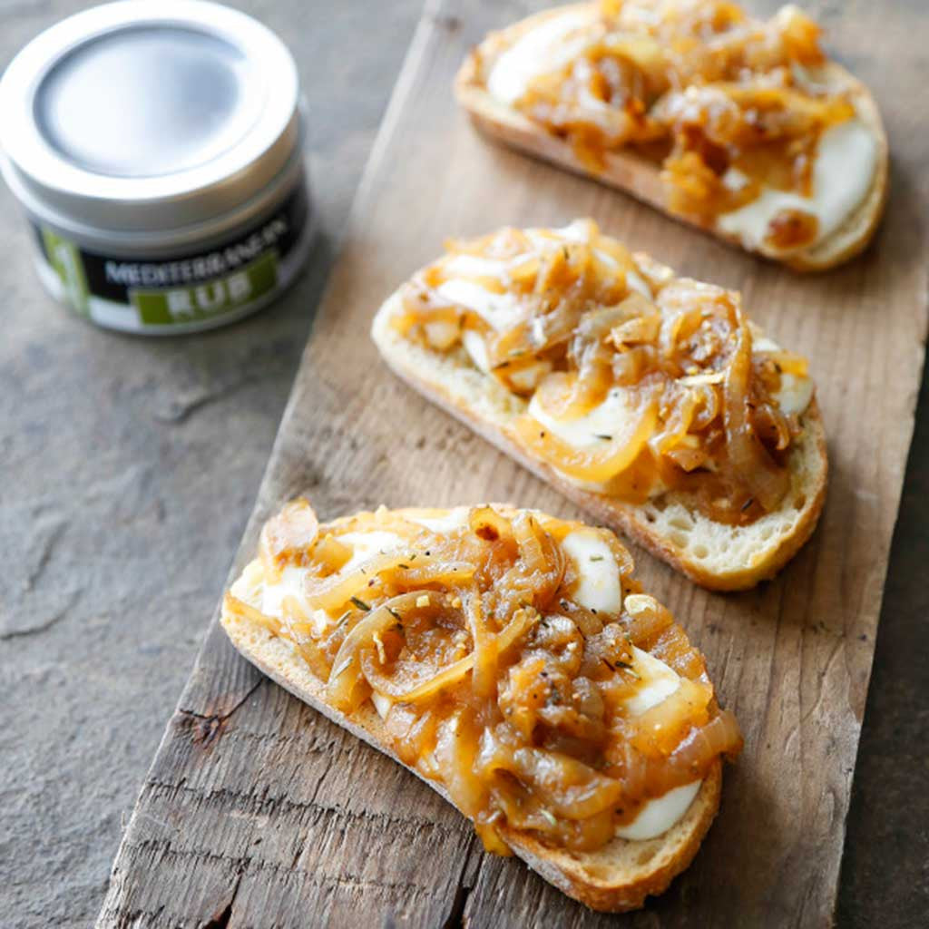 caramelized frenched onions atop melted mozzarella and crostini crackers next to a tin of Mediterranean rub seasoning