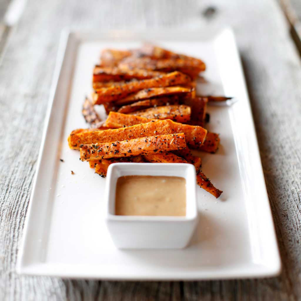 Coffee Roasted Sweet Potato Fries with Smoked Maple Aioli served on a white platter on a wooden table top.