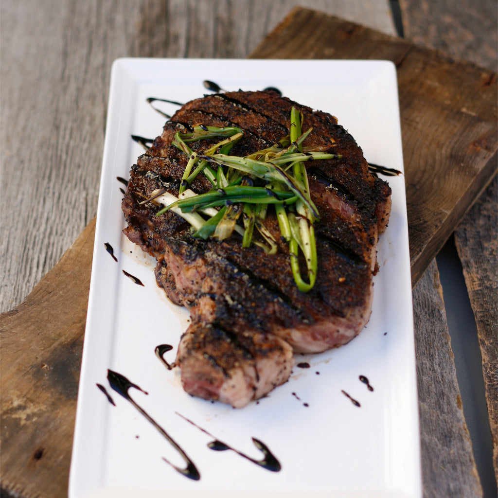 A coffee grilled ribeye steak made with smoked balsamic glaze served on a white rectangular plate and garnished with grilled green onions