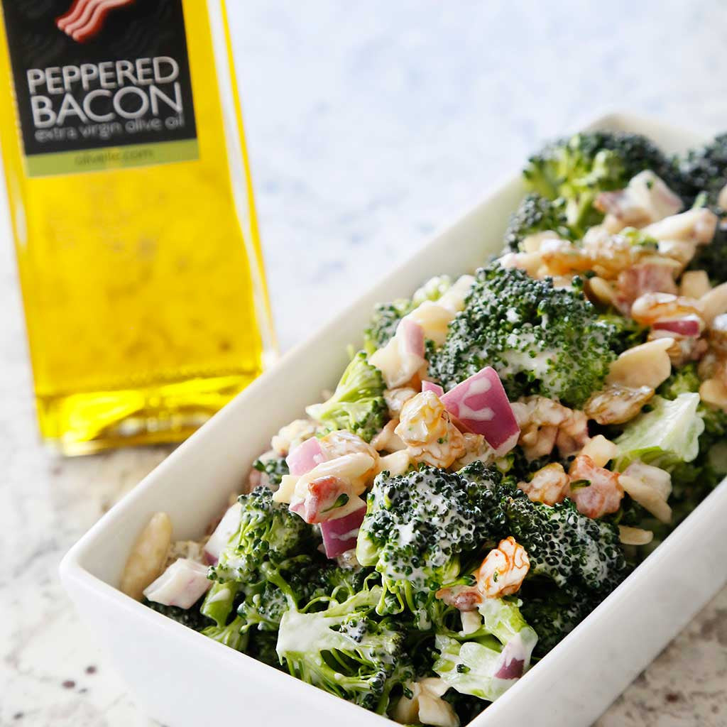 Creamy Bacon Broccoli Salad with golden raisins, purple onion and peppered bacon infused olive oil in a rectangular white dish on a marble counter top.