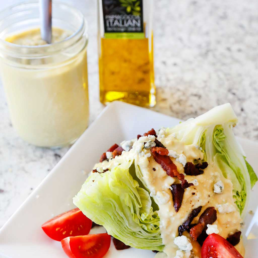 Blue Cheese Dressing with a Classic Wedge Salad made with iceberg lettuce and topped with the dressing, tomatoes, blue cheese crumbles and crumbled bacon, while sprinkled with salt and pepper and served next to a mason jar of dressing and a bottle of oil