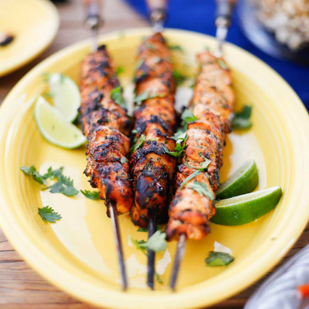 Honey Lime Chicken Skewers with slices of lime on the side. served on a yellow platter