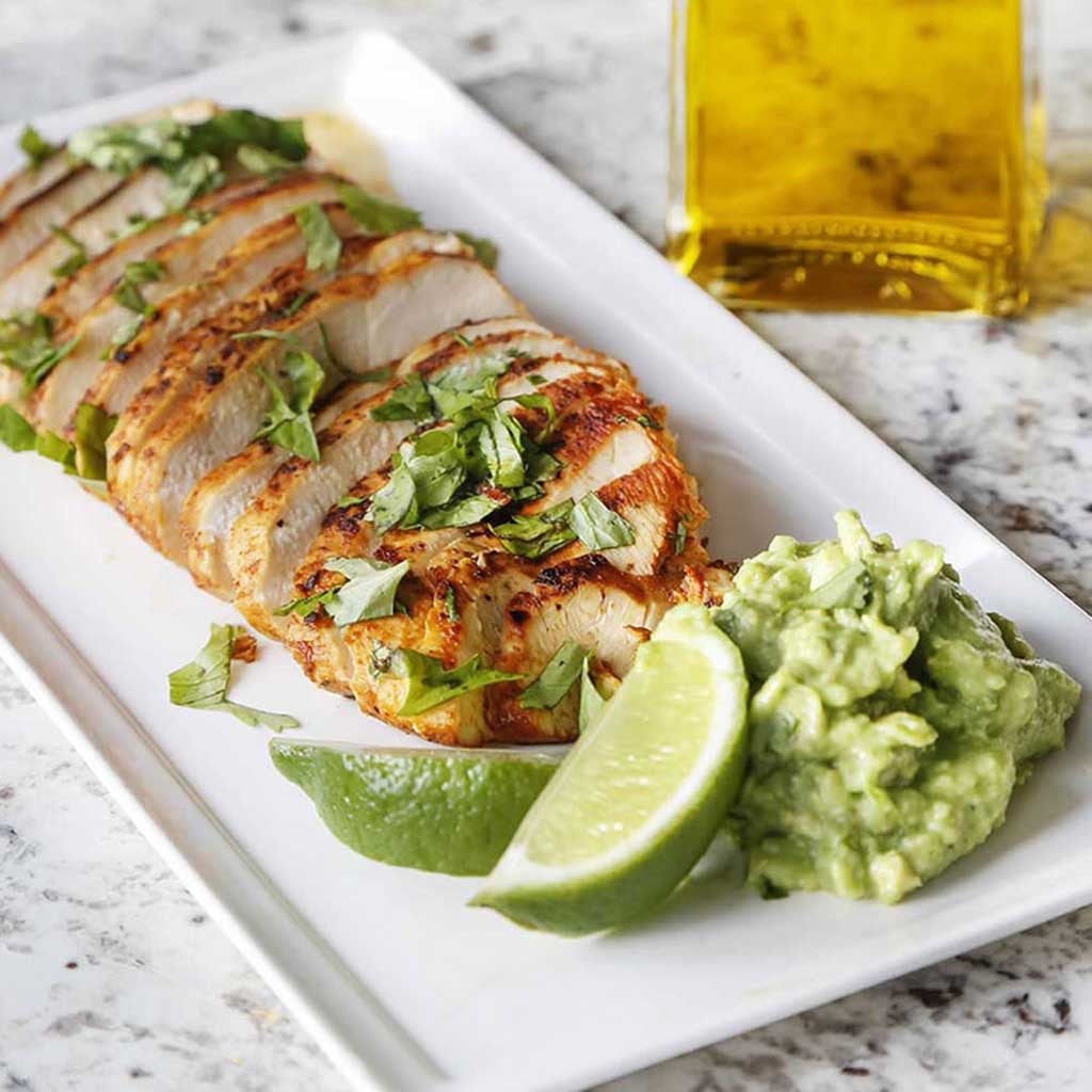 marinated mexican lime chicken with cilantro, limes, and guacamole on square white plate on top of a marble table top