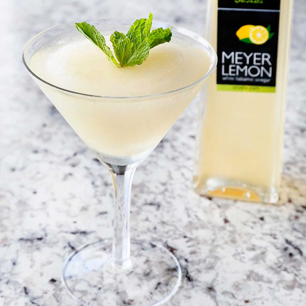 Meyer Lemon Sorbet served in a martini glass garnished with mint next to a bottle of Meyer Lemon Balsamic Vinegar atop a granite countertop