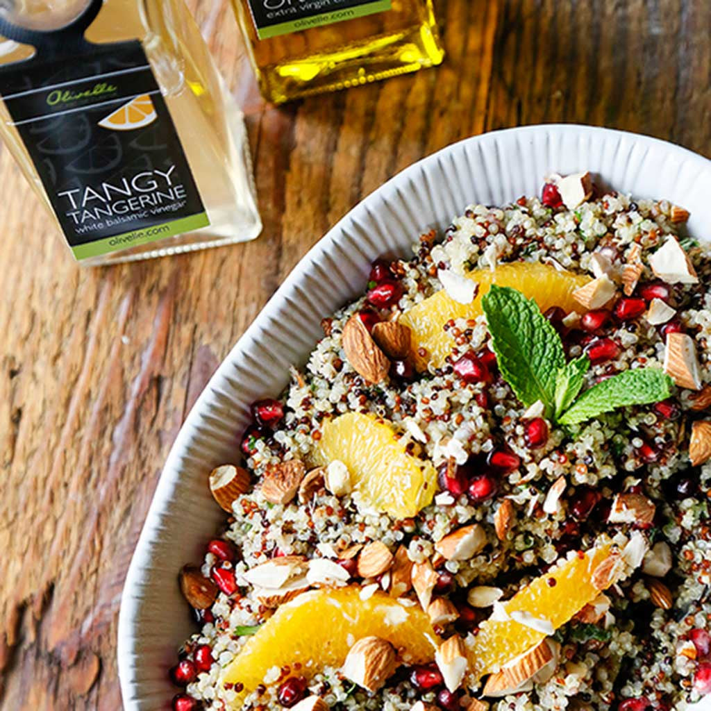 A colorful Pomegranate Citrus Quinoa Salad served in a white platter next to a bottle of tangerine white balsamic vinegar 