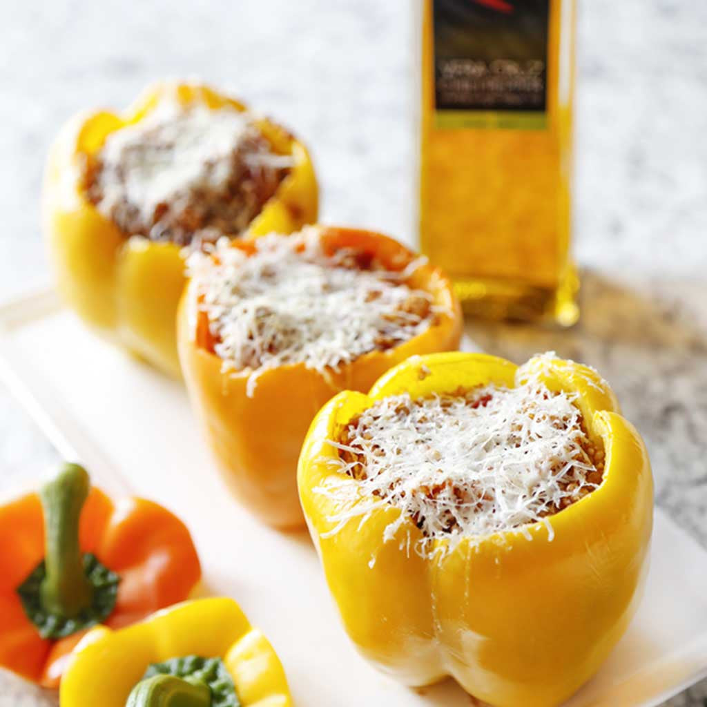 yellow and orange peppers stuffed with mexican quinoa and topped with pecorino cheese alongside veracruz chili olive oil and bell peppers served on a white platter on a marble table top