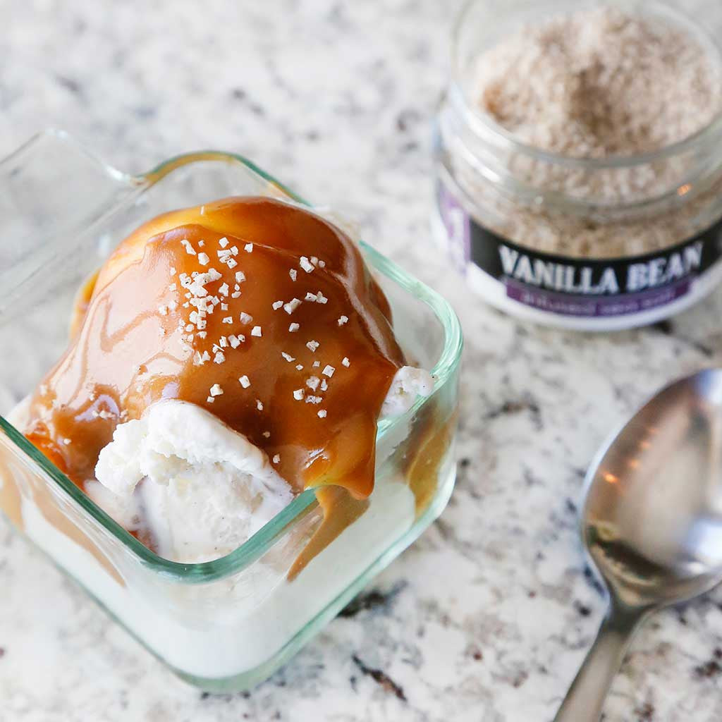 Salted honey caramel sauce is perfect to serve over your vanilla ice cream or brownies made with honey, brown sugar, half and half, butter, vanilla bean sea salt and vanilla extract. Served here over ice cream in a glass dish alongside a spoon.