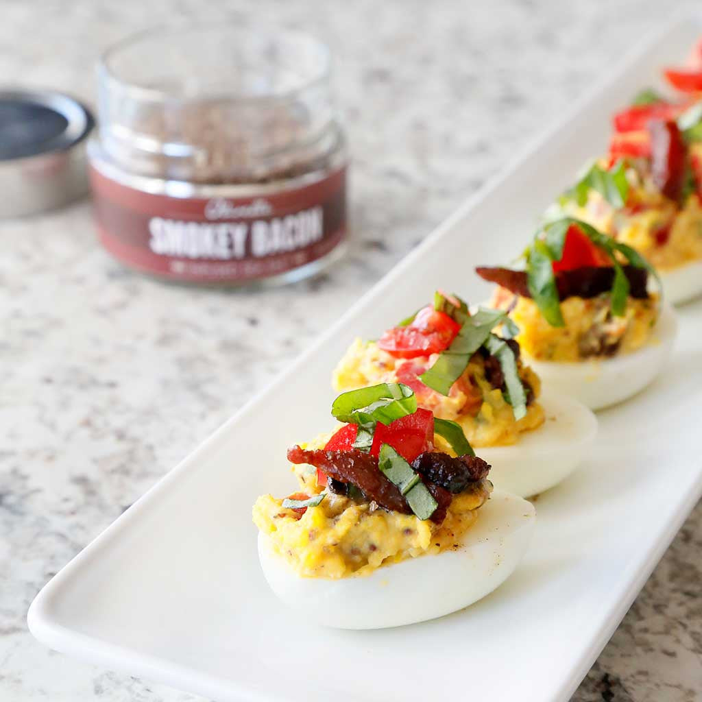 blt deviled eggs with bacon, basil, and tomato on rectangular white plate alongside smokey bacon sea salt