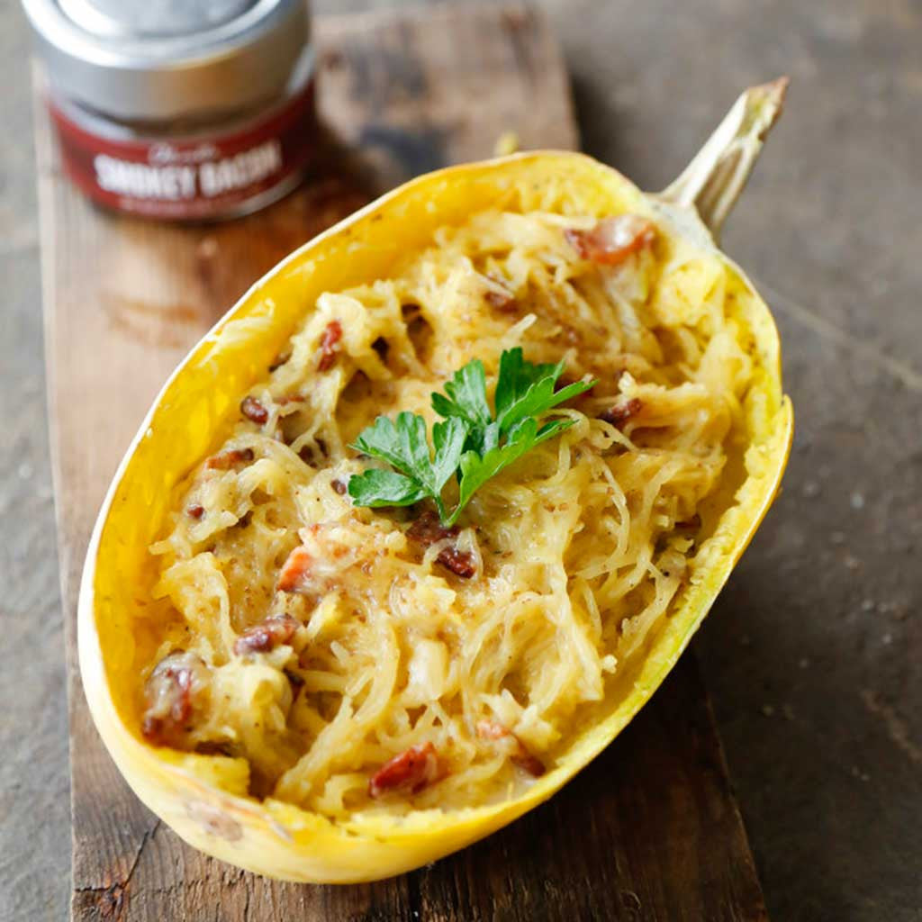 Yellow spaghetti squash carbonara with spicy bacon sea salt garnished with parsley and served next to a jar of smokey bacon sea salt