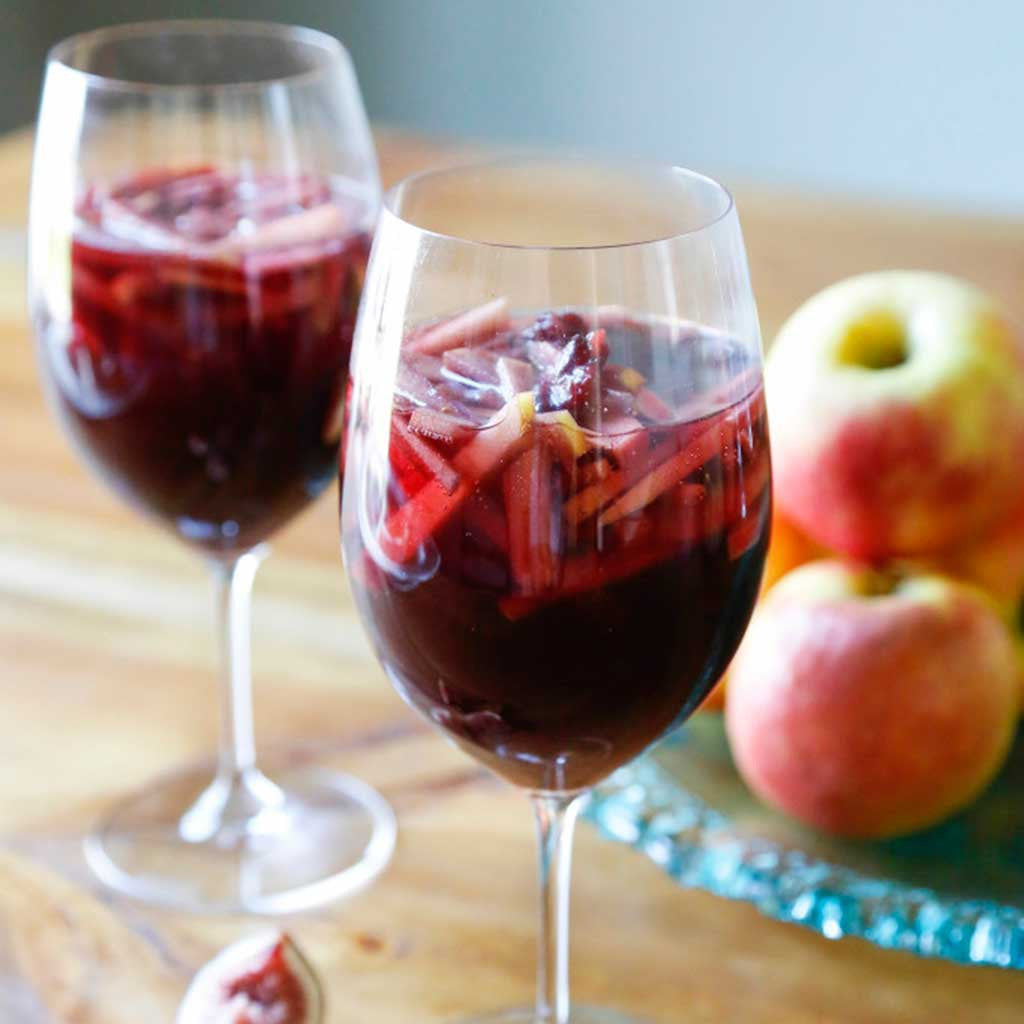 Two Spiced Apple Sparkling Sangria glasses served next to a platter of apples