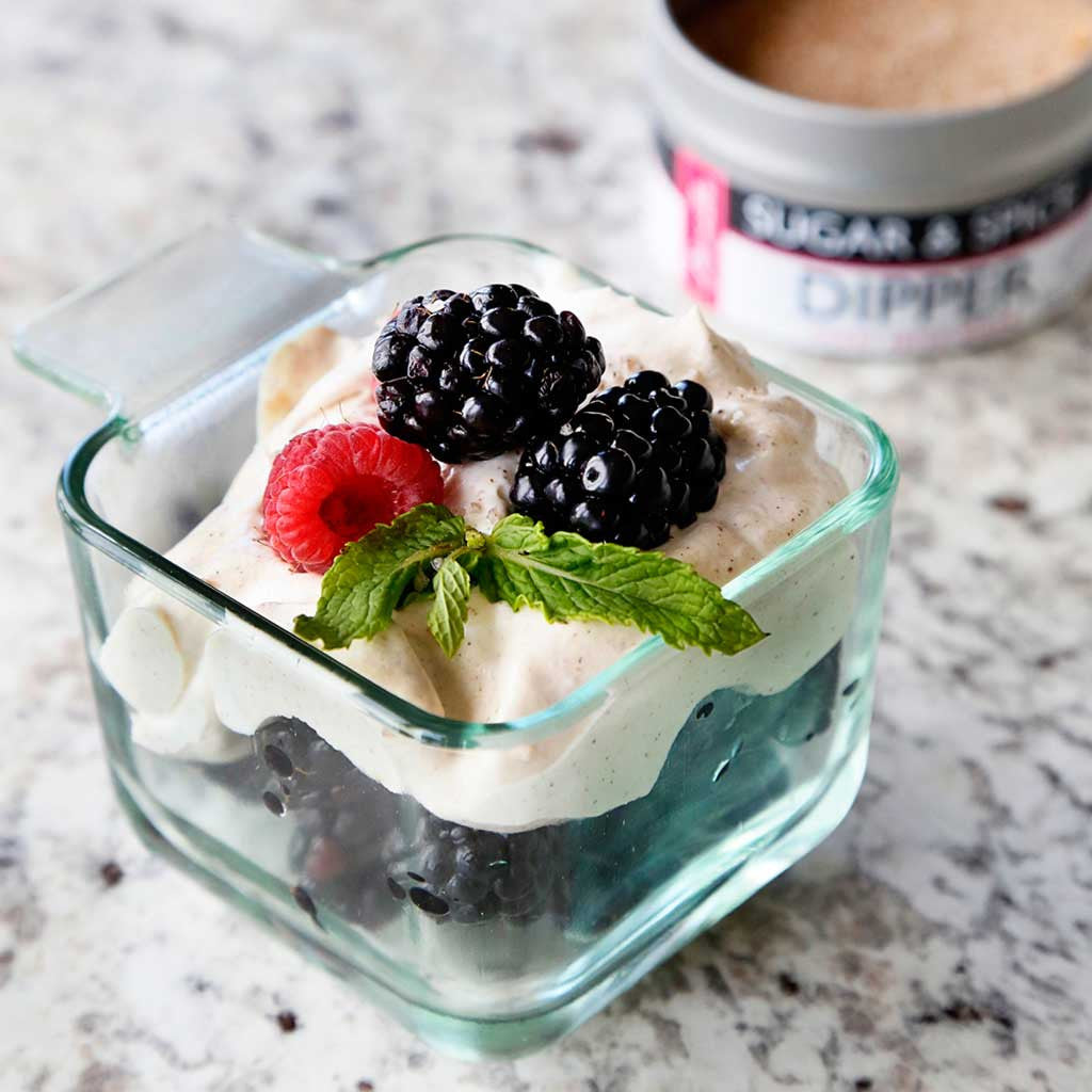 spiced italian custard served over berries in a glass square dish garnished with mint, blackberries and raspberries served next to an open jar of sugar and spice dipper