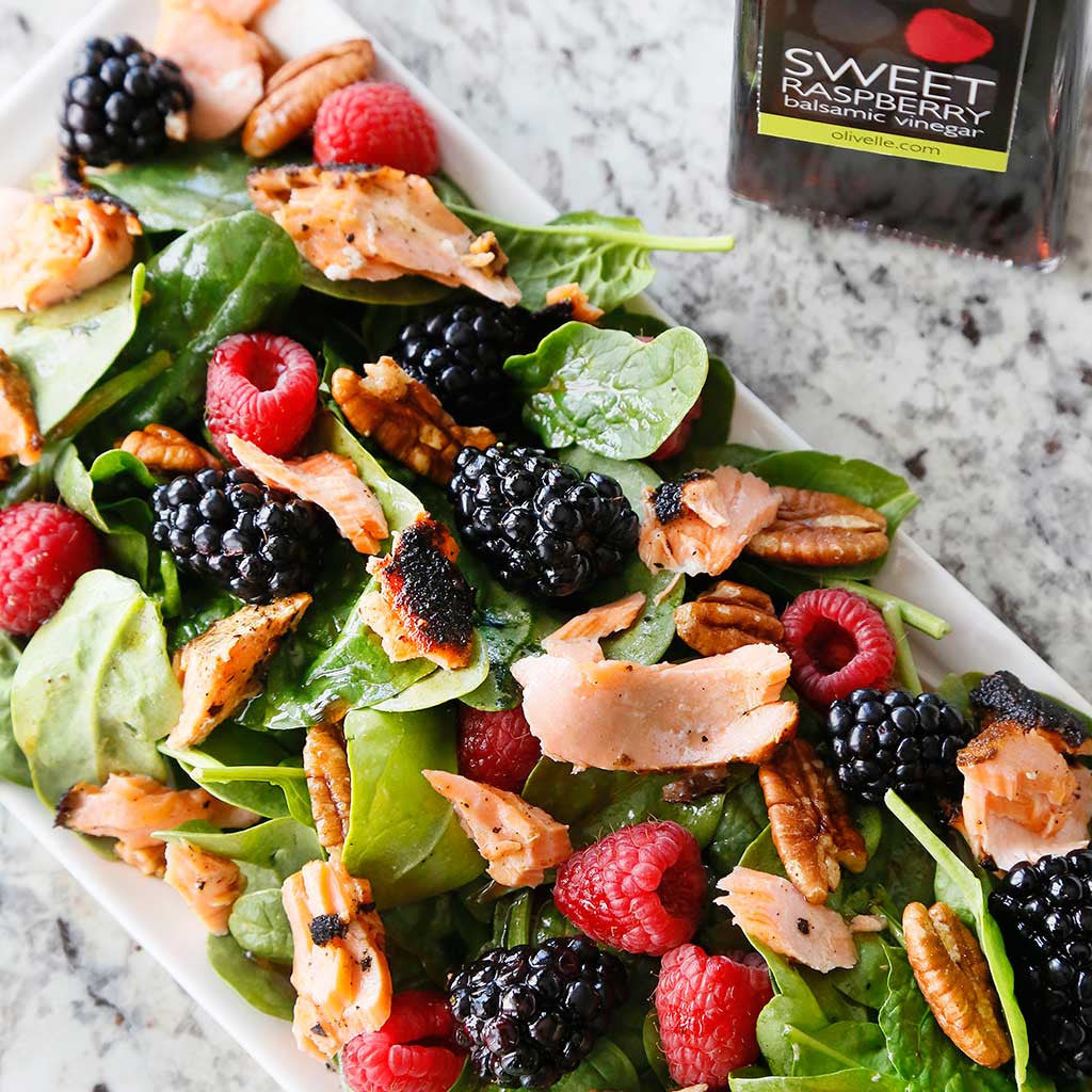 blackened salmon salad with blackberries, raspberries and pecans alongside a bottle of raspberry balsamic vinegar all on a marble counter top 