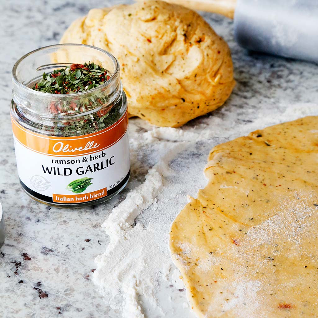 pizza dough rolled out in flour on a marble table top with a jar of wild garlic dried herb blend seasoning