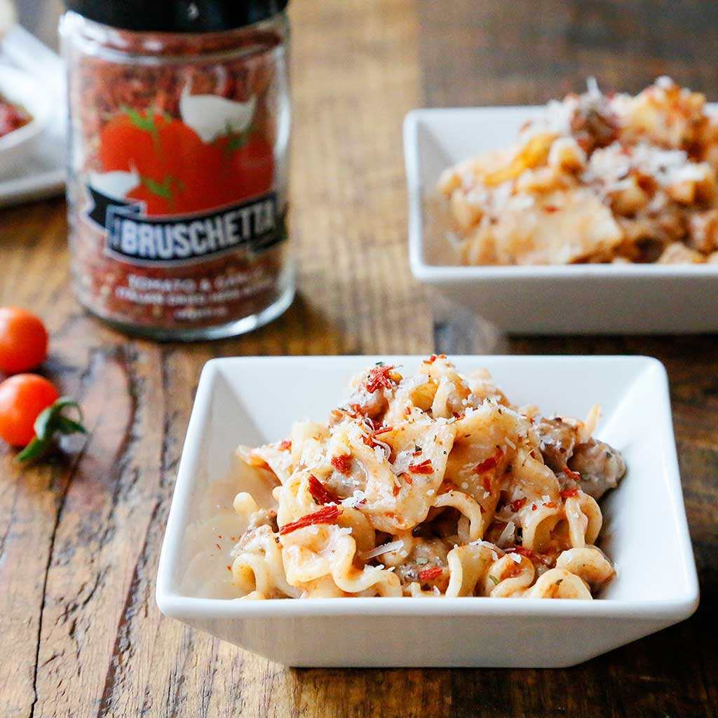 Drunken Bruschetta & Sausage Pasta served in a white square bowl next to a jar of Bruschetta Dried Herb Blend