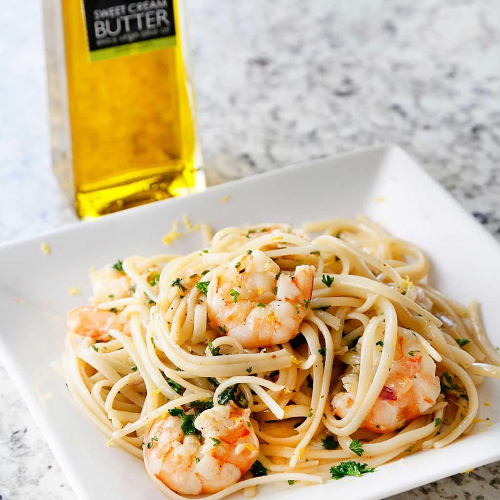 Shrimp Scampi served on a square white plate next to a bottle of Sweet Cream Butter Olive Oil on a marble counter top